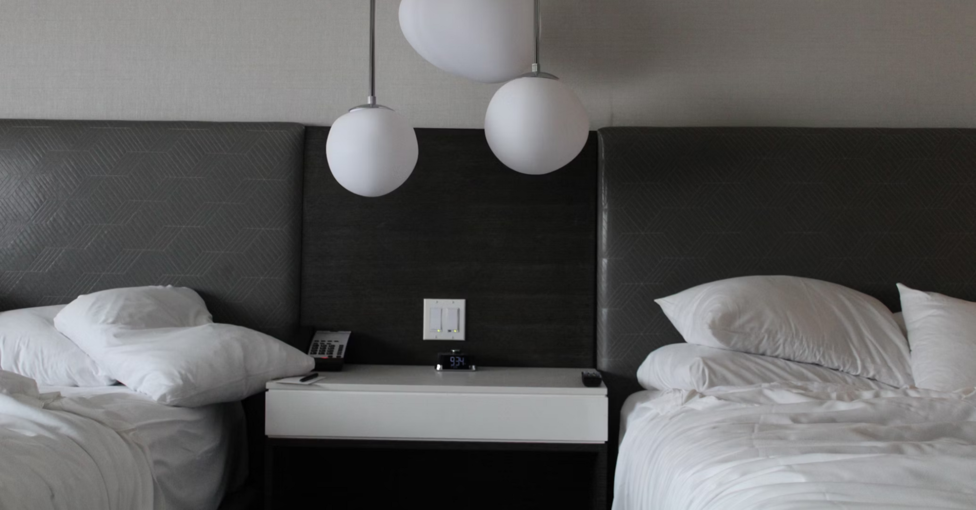Modern hotel room with two unmade beds and abstract pendant lighting