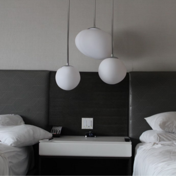 Modern hotel room with two unmade beds and abstract pendant lighting