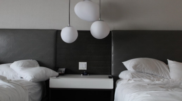 Modern hotel room with two unmade beds and abstract pendant lighting