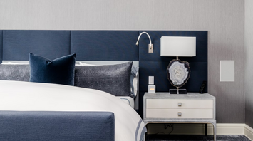 Modern hotel bedroom with navy and grey decor, featuring a neatly made bed and nightstand