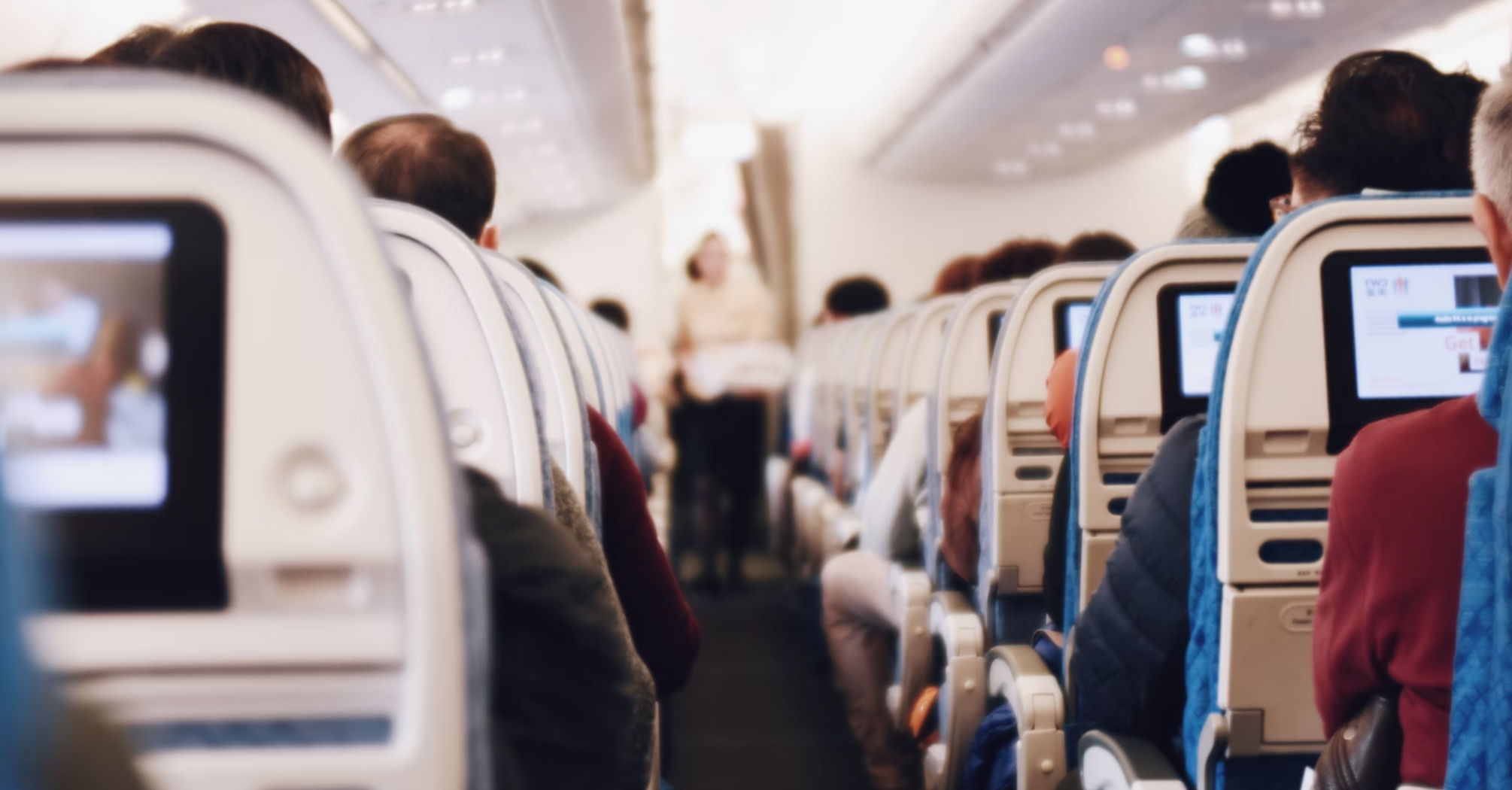 Passengers seated inside an aircraft cabin with seatback screens visible