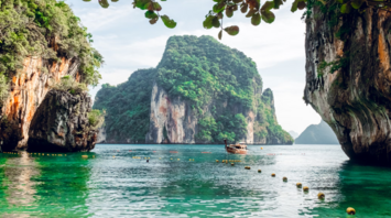 Scenic view of a traditional boat near limestone cliffs and clear green water in Krabi