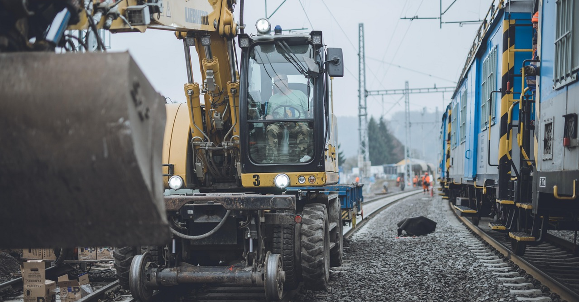 Construction vehicle working on railway tracks near stationary train