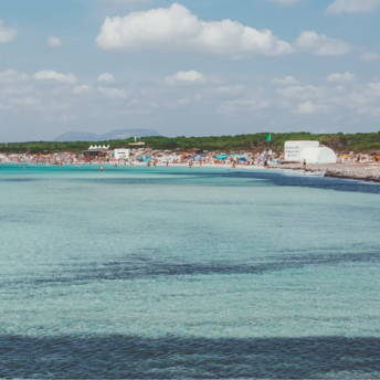 Beachgoers crowd a popular beach on a Balearic Island under a sunny sky