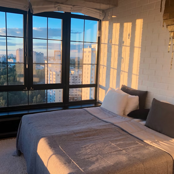 Modern bedroom with large windows and city view at sunset