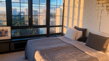 Modern bedroom with large windows and city view at sunset