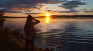 Person photographing the sunset over a calm lake in Finland during summer