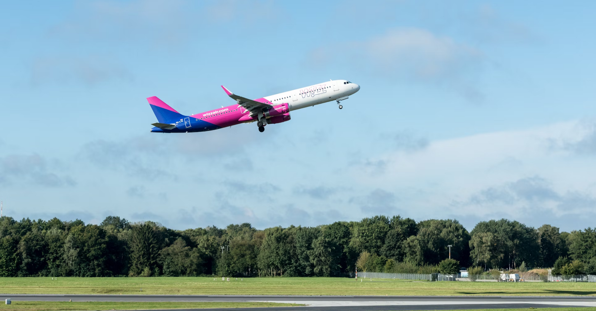 Wizz Air aircraft taking off from a runway with trees in the background