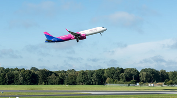Wizz Air aircraft taking off from a runway with trees in the background