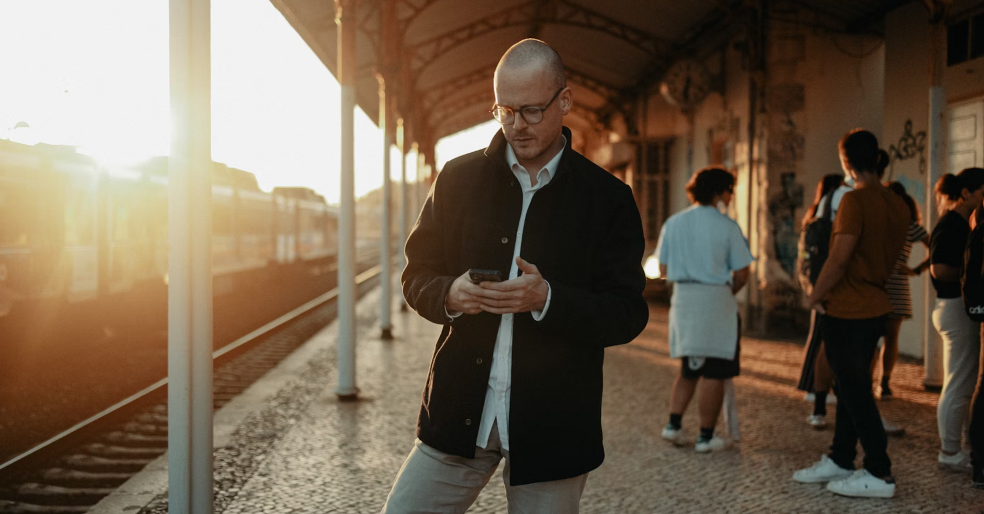 Man checking phone at train station during sunset