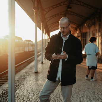 Man checking phone at train station during sunset