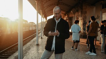 Man checking phone at train station during sunset