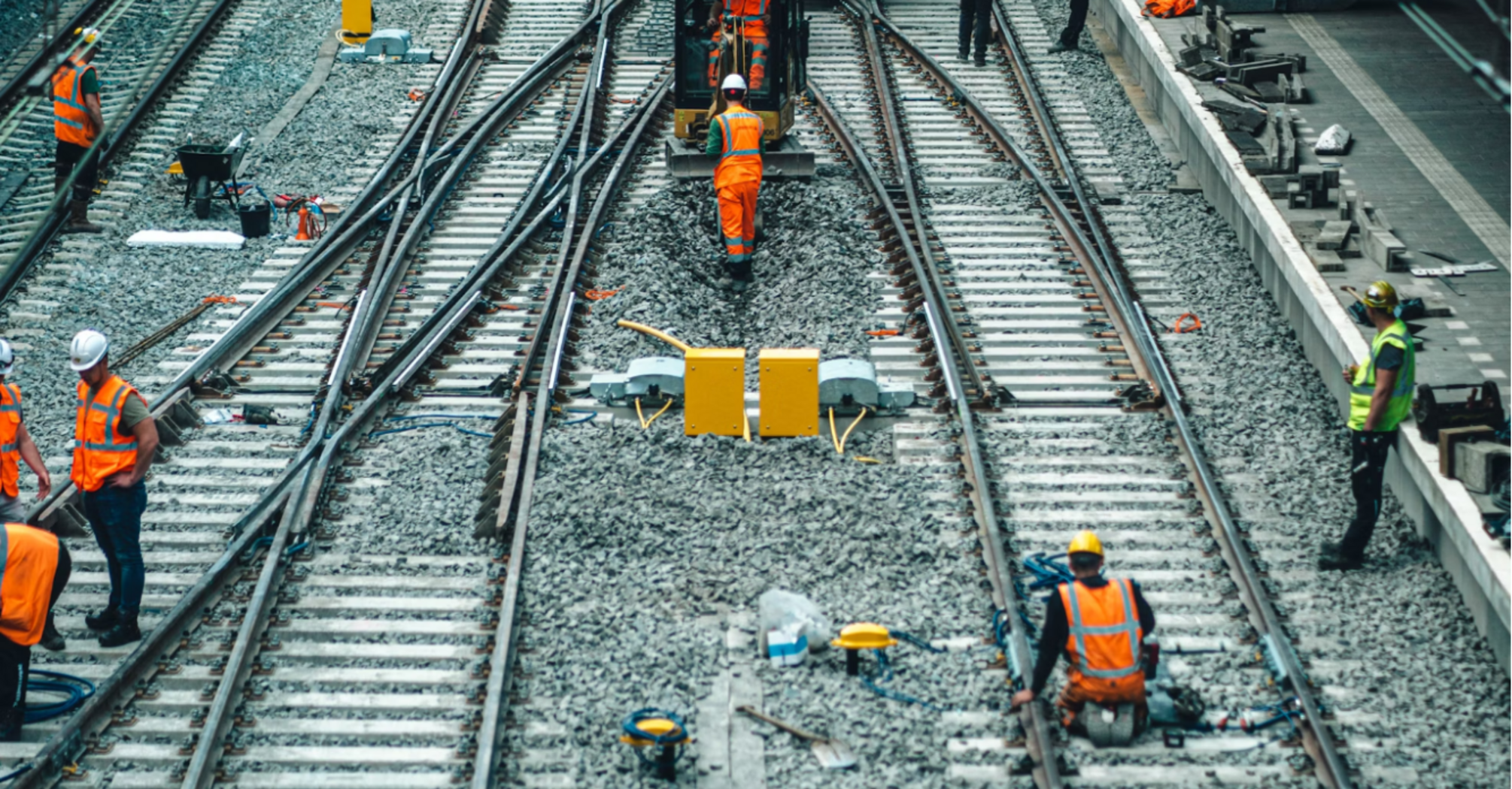 Rail workers conducting track and signal maintenance at a train station during daylight hours