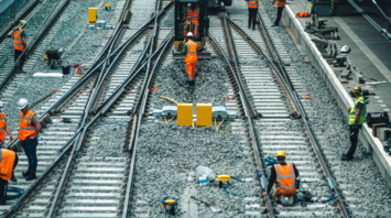 Rail workers conducting track and signal maintenance at a train station during daylight hours