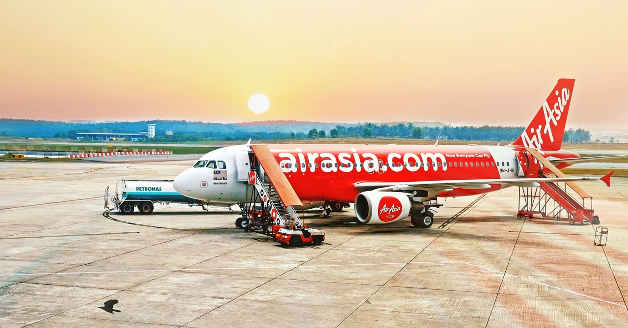 AirAsia aircraft on tarmac during sunrise with boarding stairs and fuel truck nearby