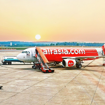AirAsia aircraft on tarmac during sunrise with boarding stairs and fuel truck nearby