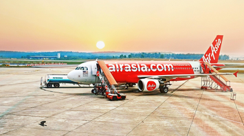 AirAsia aircraft on tarmac during sunrise with boarding stairs and fuel truck nearby