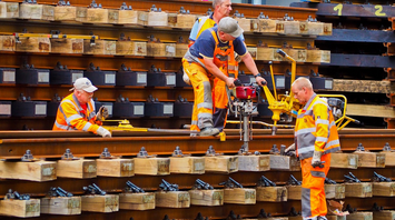 Workers in safety gear repairing railway tracks with heavy equipment