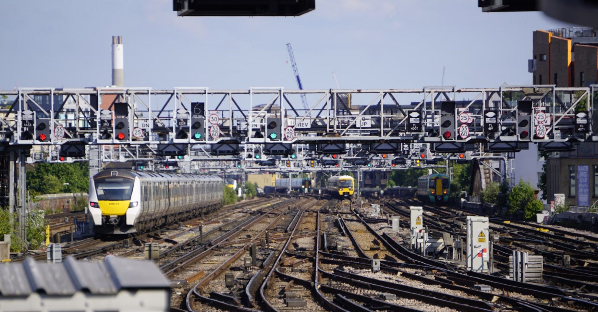 Multiple trains approach a busy London rail junction under a canopy of signals