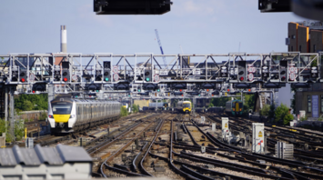 Multiple trains approach a busy London rail junction under a canopy of signals