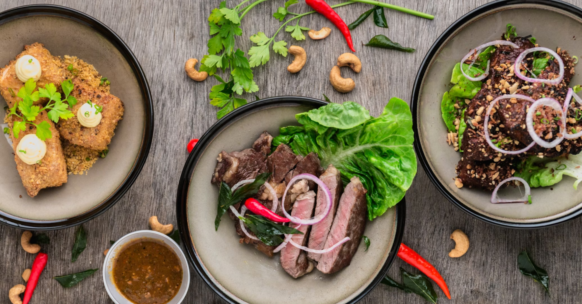 Three diverse dishes served in food hall style with herbs and spices