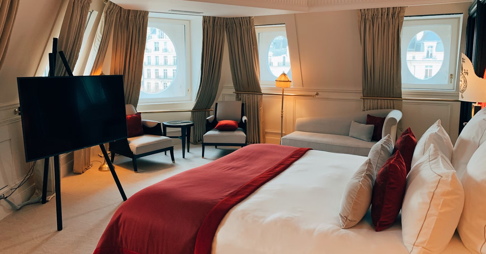 Luxury hotel suite with round windows, red bedding, and city view