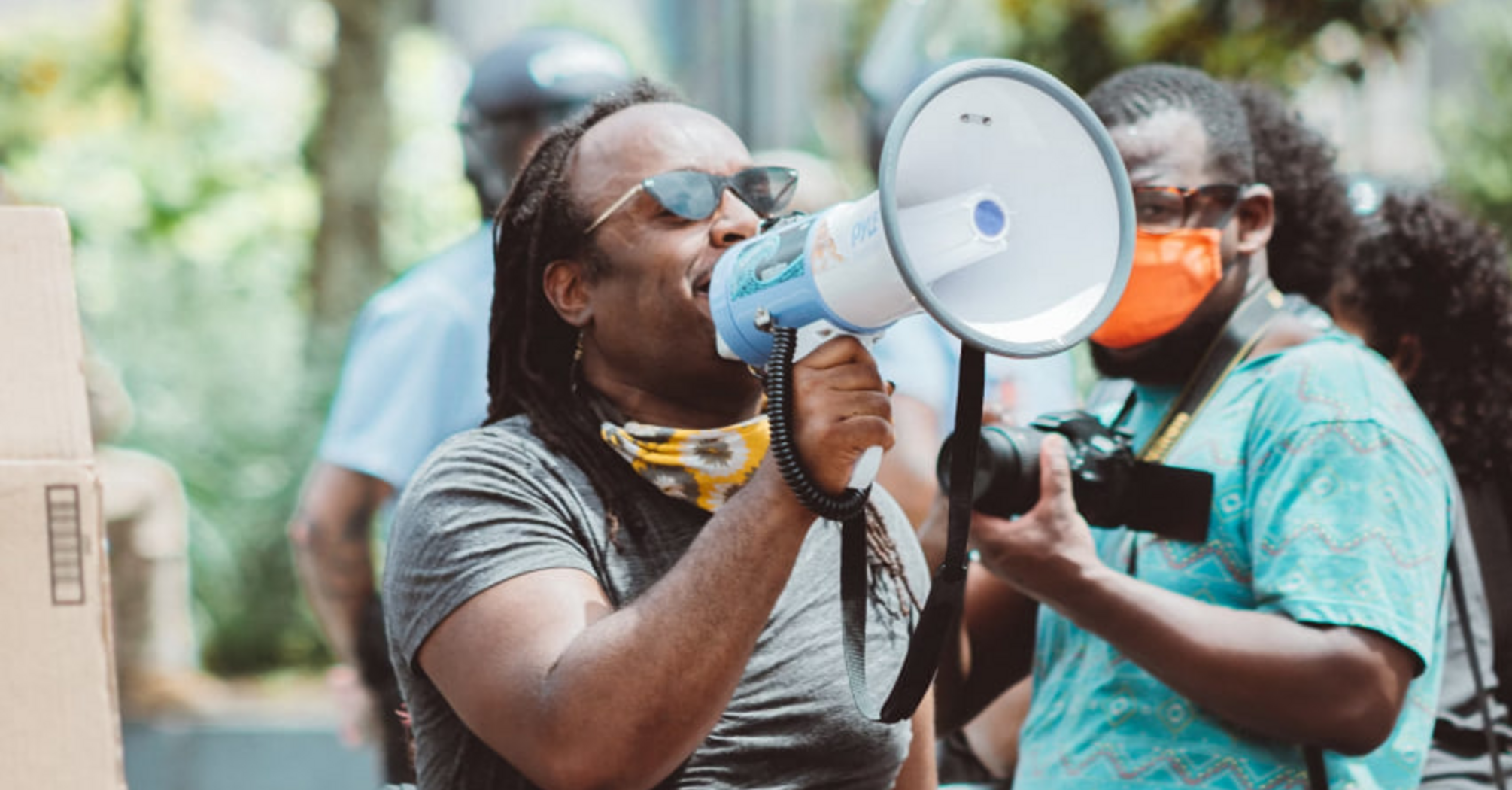A person speaking through a megaphone during a protest, surrounded by others