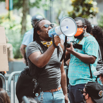 A person speaking through a megaphone during a protest, surrounded by others