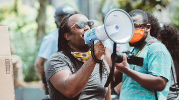 A person speaking through a megaphone during a protest, surrounded by others