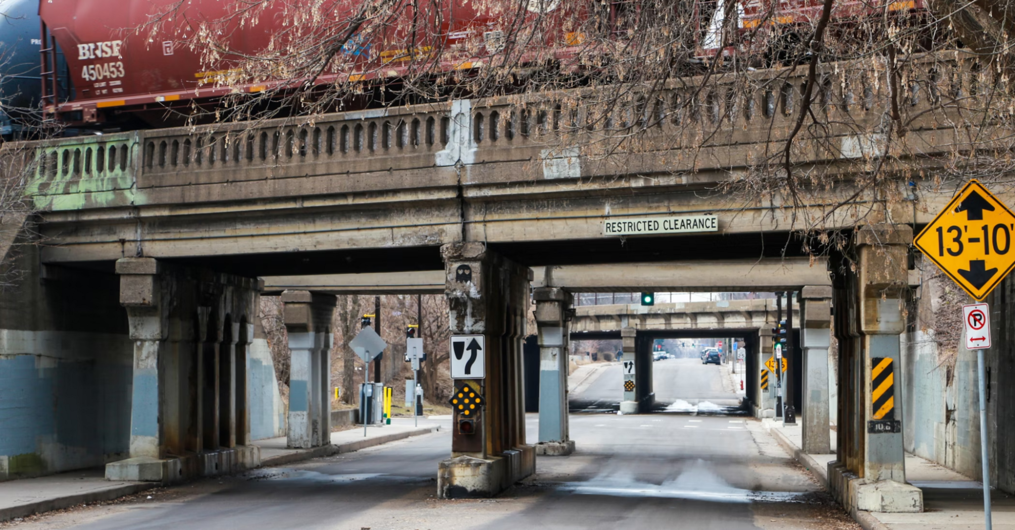 Freight train crossing an old bridge over a narrow road with restricted clearance signs