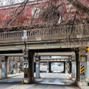 Freight train crossing an old bridge over a narrow road with restricted clearance signs