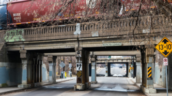 Freight train crossing an old bridge over a narrow road with restricted clearance signs