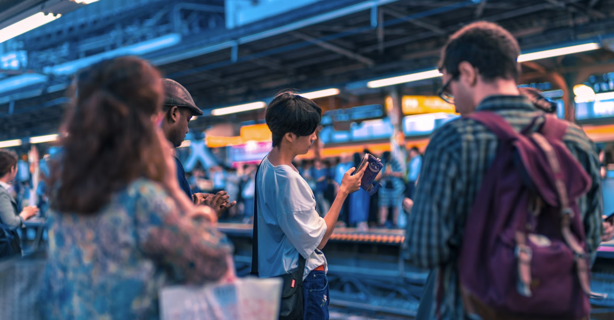 Commuters checking their phones while waiting at a busy train platform
