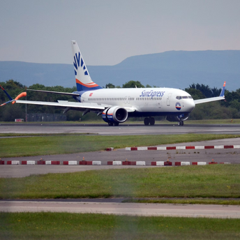 A SunExpress airplane taxiing on the runway at an airport with green hills in the background