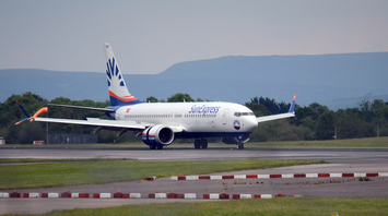 A SunExpress airplane taxiing on the runway at an airport with green hills in the background