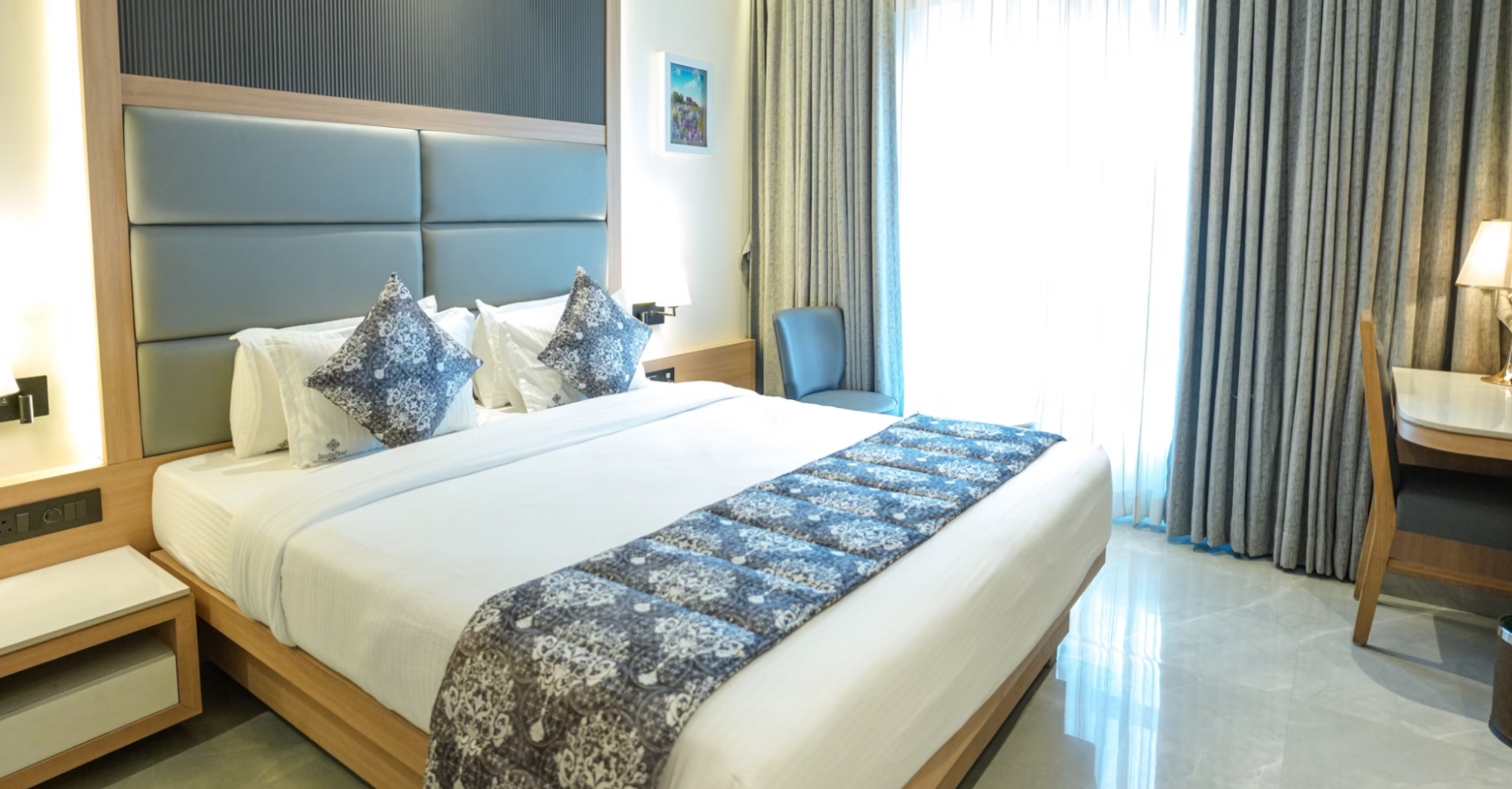 Modern hotel room with large bed, soft lighting, and work desk
