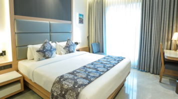 Modern hotel room with large bed, soft lighting, and work desk