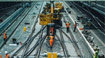 Workers in high-visibility gear conduct railway maintenance using machinery on a curved track under construction