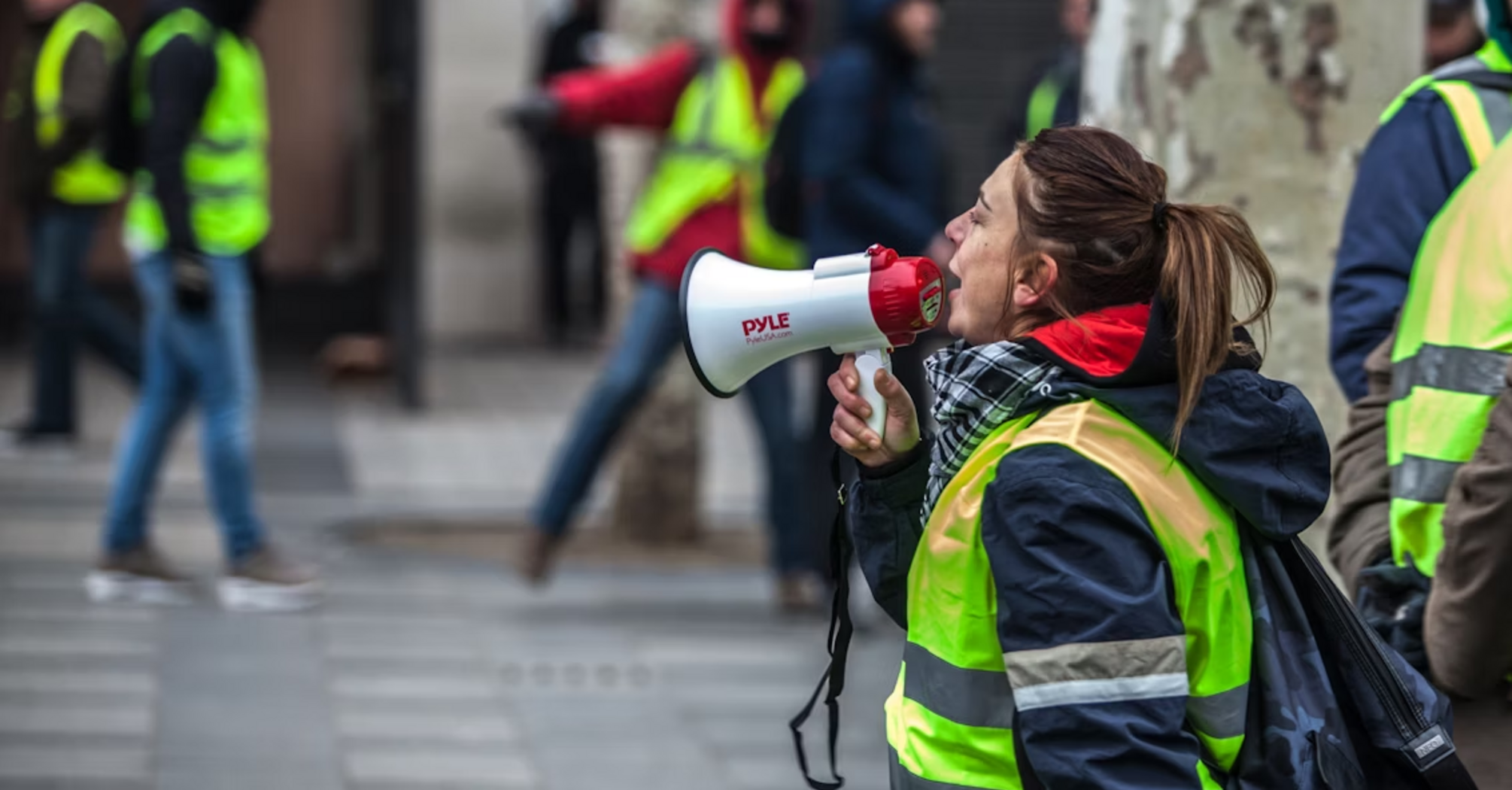Protester in high-visibility vest shouting through megaphone during a strike