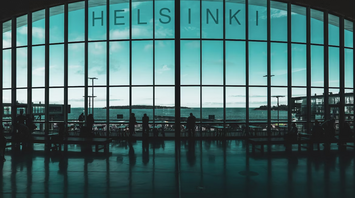 View of Helsinki Airport terminal with passengers silhouetted against large windows