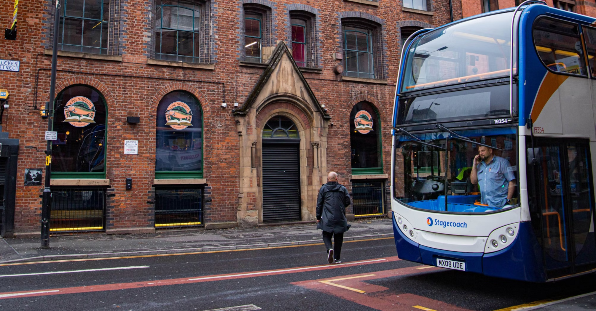 A Stagecoach double-decker bus stops on a city street in front of a historic brick building