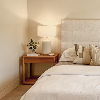 Modern hotel room corner with bedside table, lamp, and neutral bedding