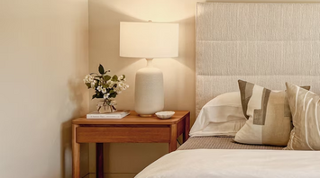 Modern hotel room corner with bedside table, lamp, and neutral bedding