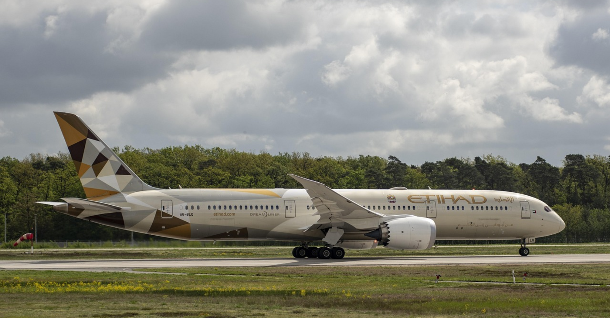 Etihad Airways aircraft taxiing on runway under cloudy sky