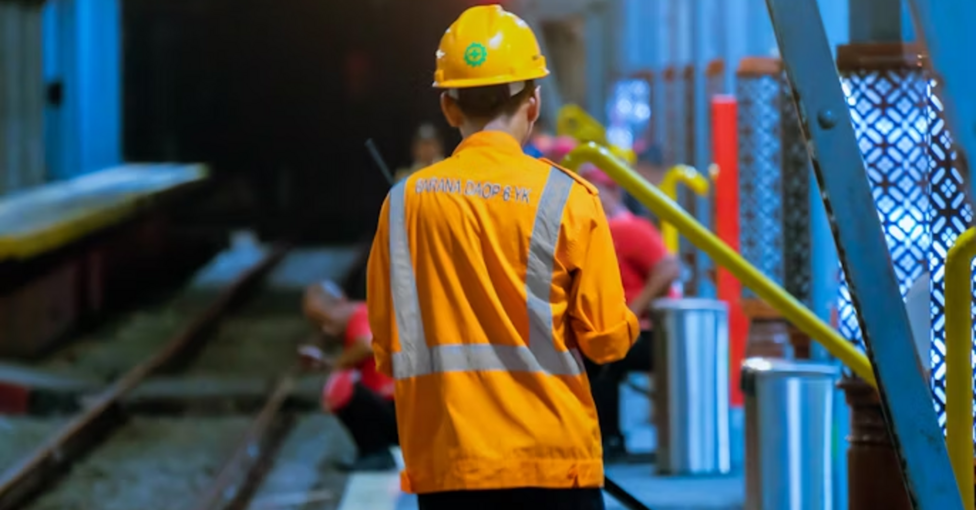 Rail worker in safety gear walking near tracks inside a tunnel