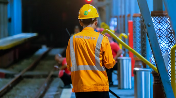 Rail worker in safety gear walking near tracks inside a tunnel