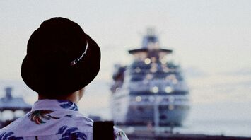 Person in tropical shirt looking at a docked cruise ship