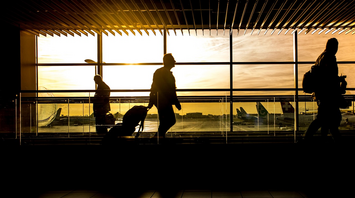 Silhouetted travelers walking through airport at sunset