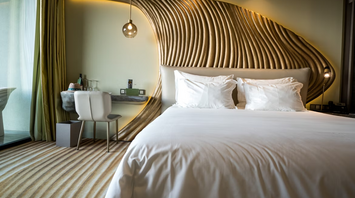 Modern hotel room with white bedding and sculptural wooden wall design