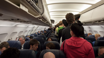 Passengers standing and sitting inside a crowded airplane cabin